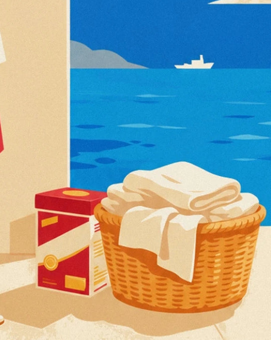 A wicker basket full of white laundry and a red box of washing powder, facing the sea and a boat