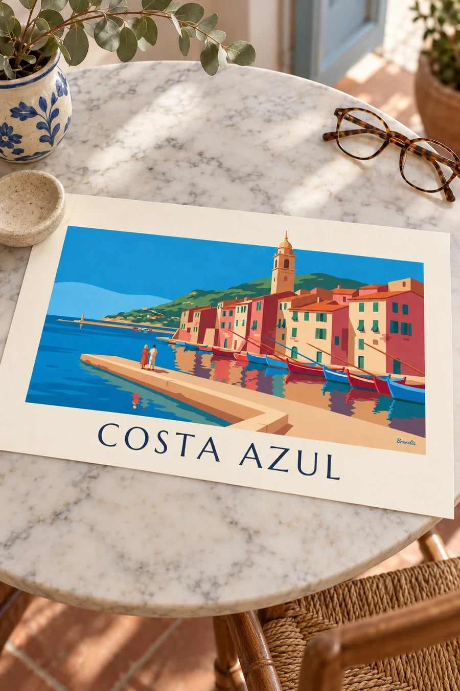 Póster de fachadas de colores y barcos de un puerto de la Costa Azul: apoyado sobre una mesa